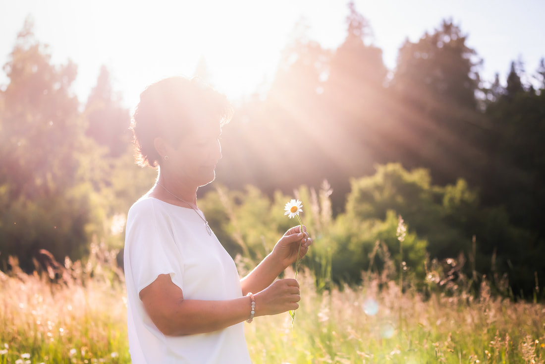 Frau hält Margaritenblume in Hand, bewundert sie achtsam in der Abendsonne, symbolisiert Bewusstseinstraining und Achtsamkeit.